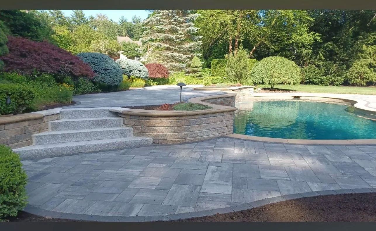 Stone patio with steps, raised garden bed, and pool surrounded by lush landscaping.