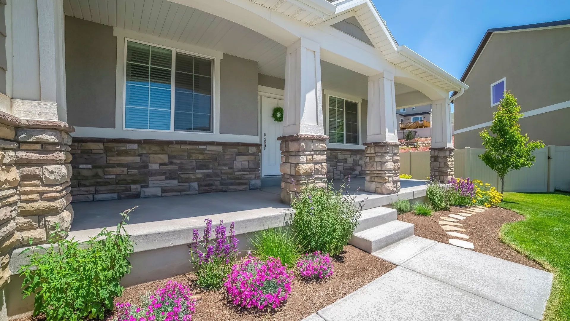 A house with stone columns, porch, and vibrant pink and purple flowers.