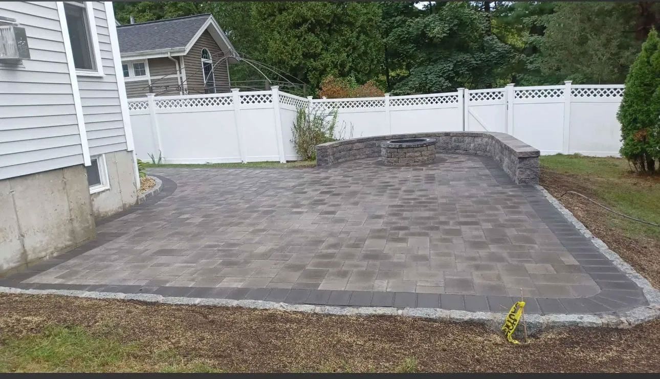 Paved patio with a retaining wall and white fence next to a house.