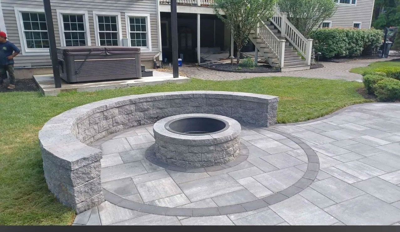 Stone fire pit with curved wall seating on a paved patio, near a house.