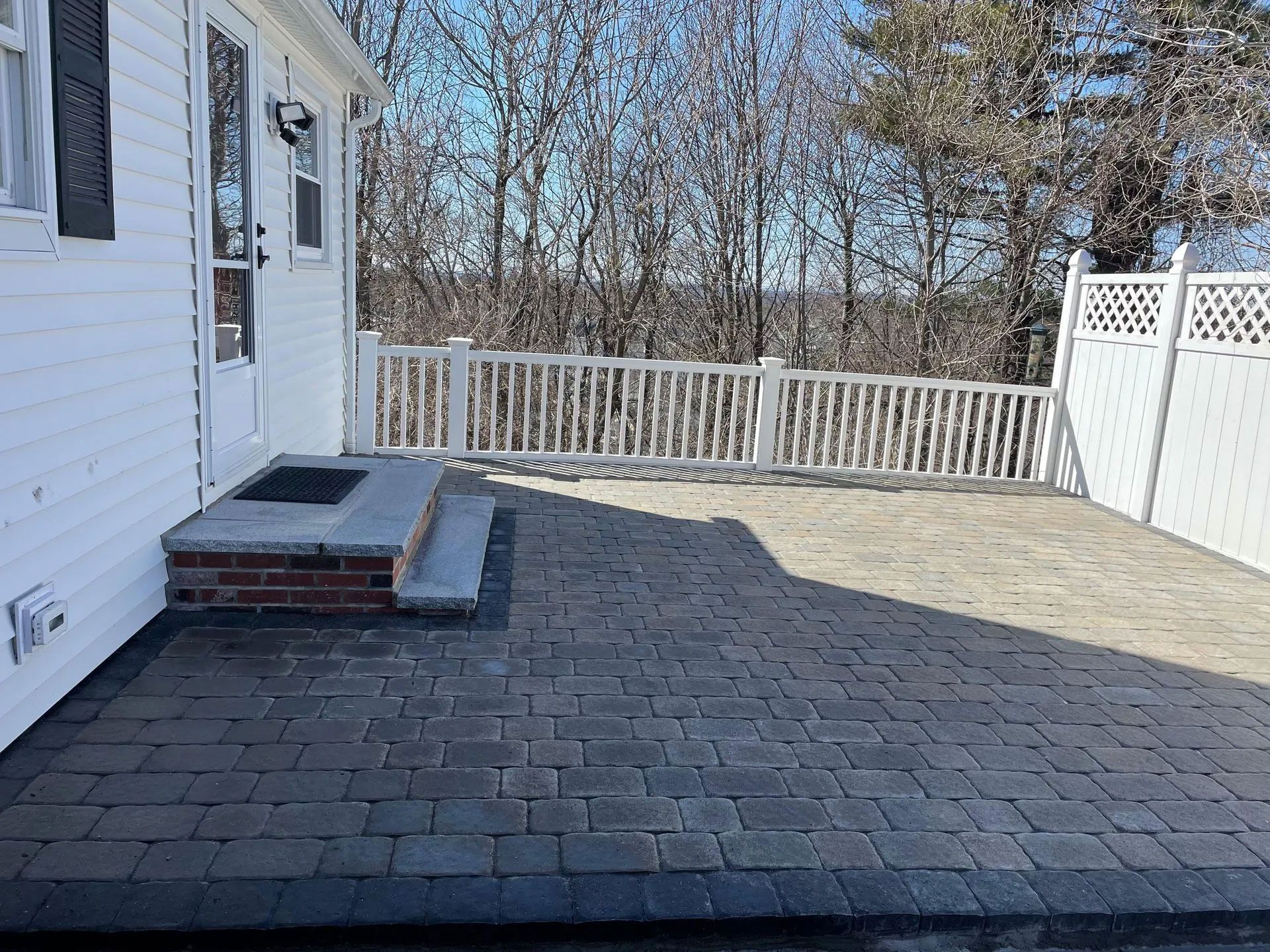 Patio with brick steps, pavers, white railing, and a white house on a sunny day.