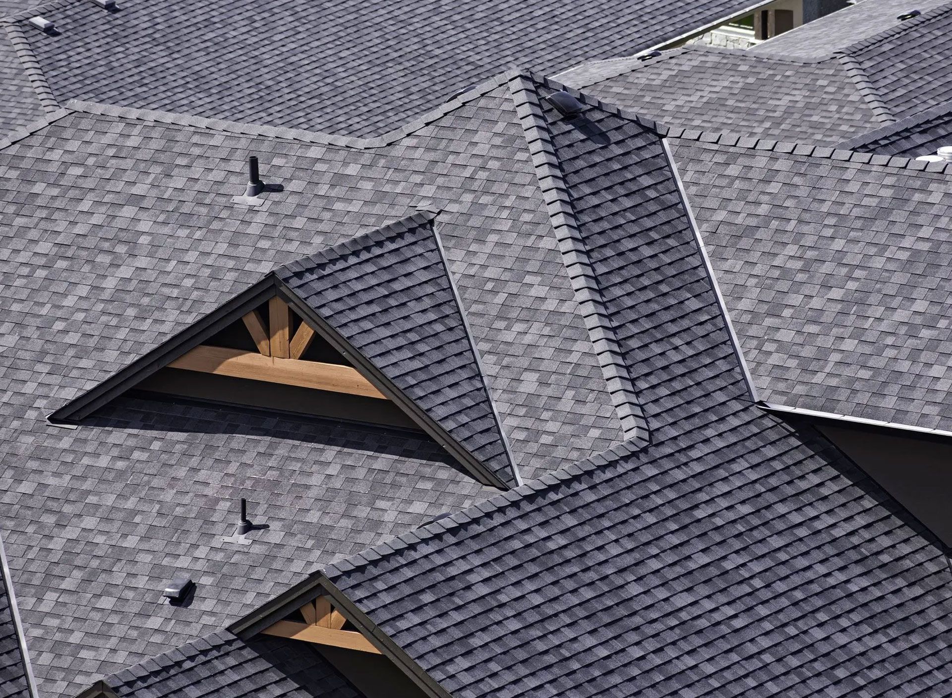 Overhead view of multiple gray shingled roofs with wooden supports and vents.
