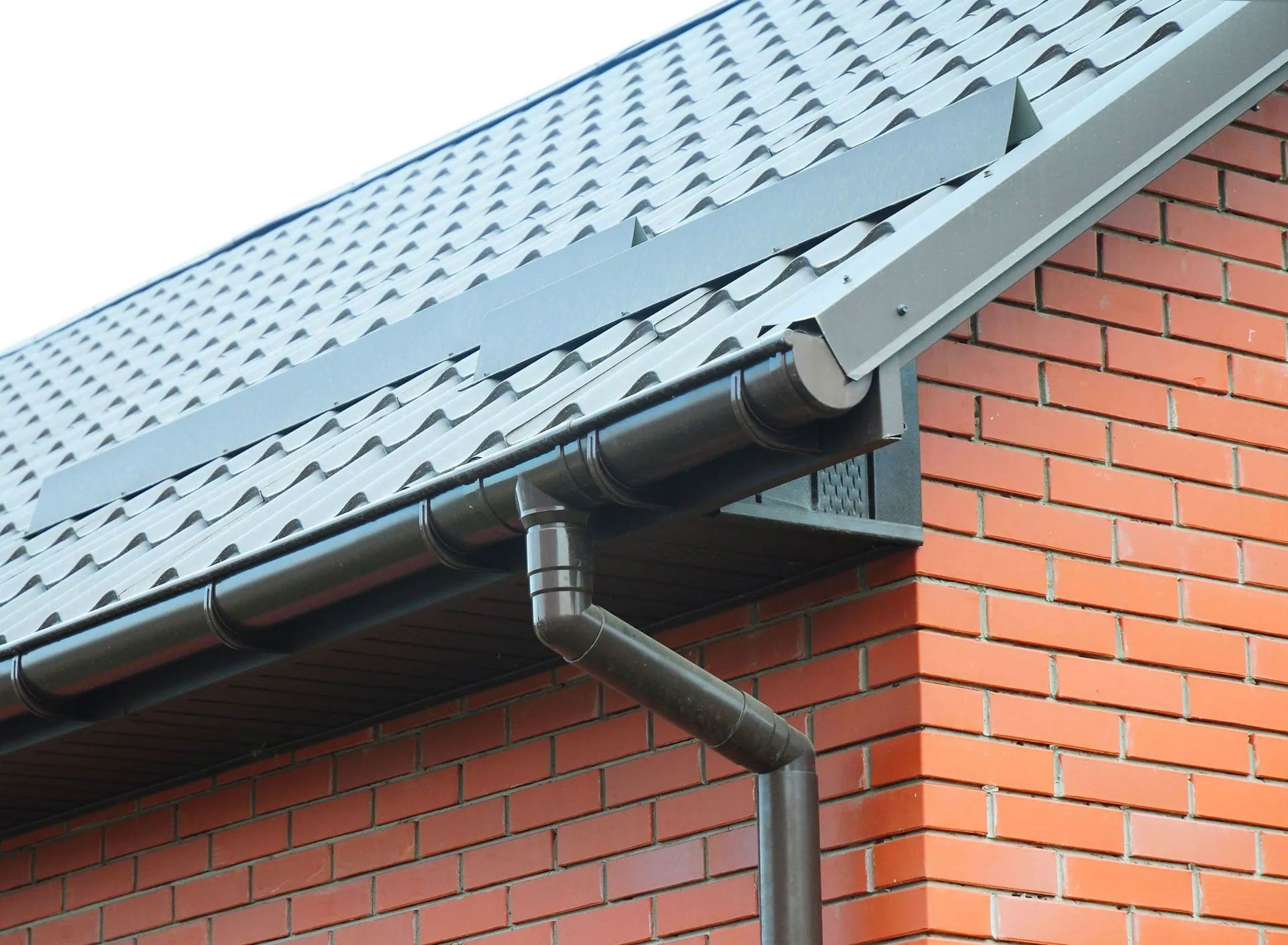 Brown gutters and downspout on a red brick building with gray roof tiles.
