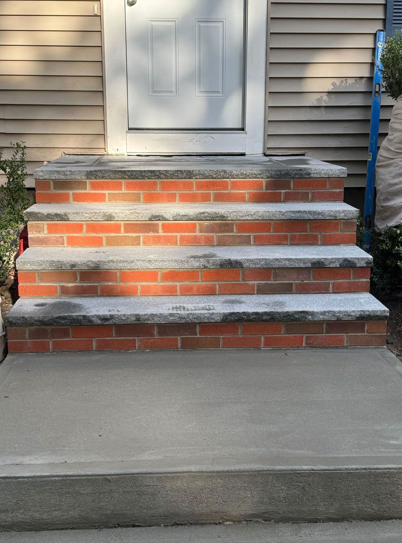 Brick and concrete steps leading to a white door. Brick is red, concrete is gray.