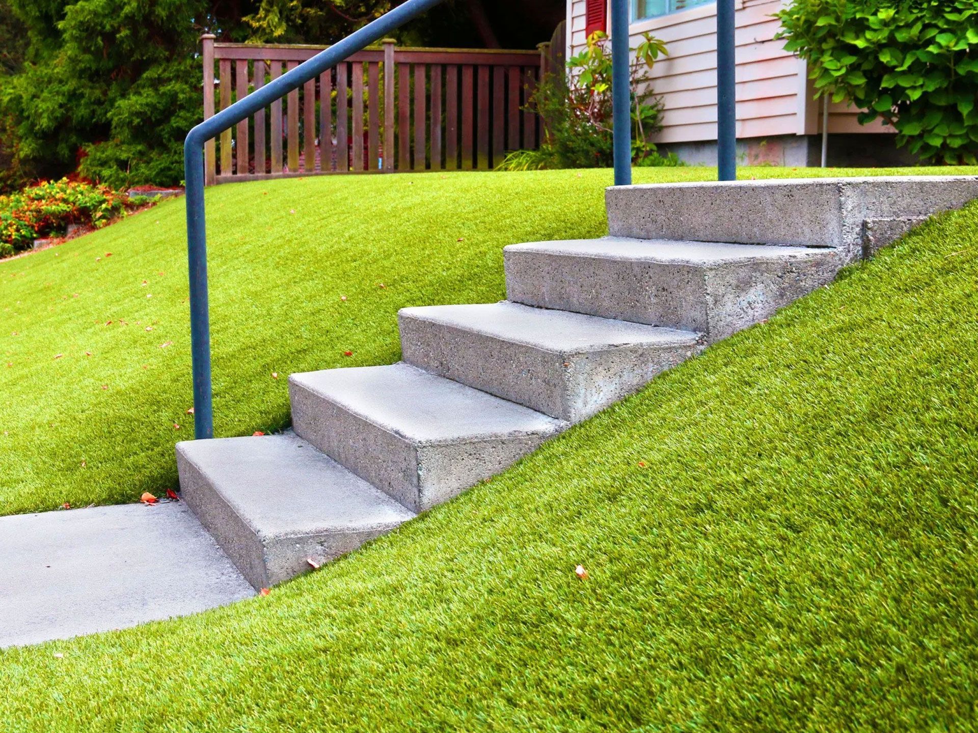 Concrete steps leading up a grassy hill, with a blue handrail.