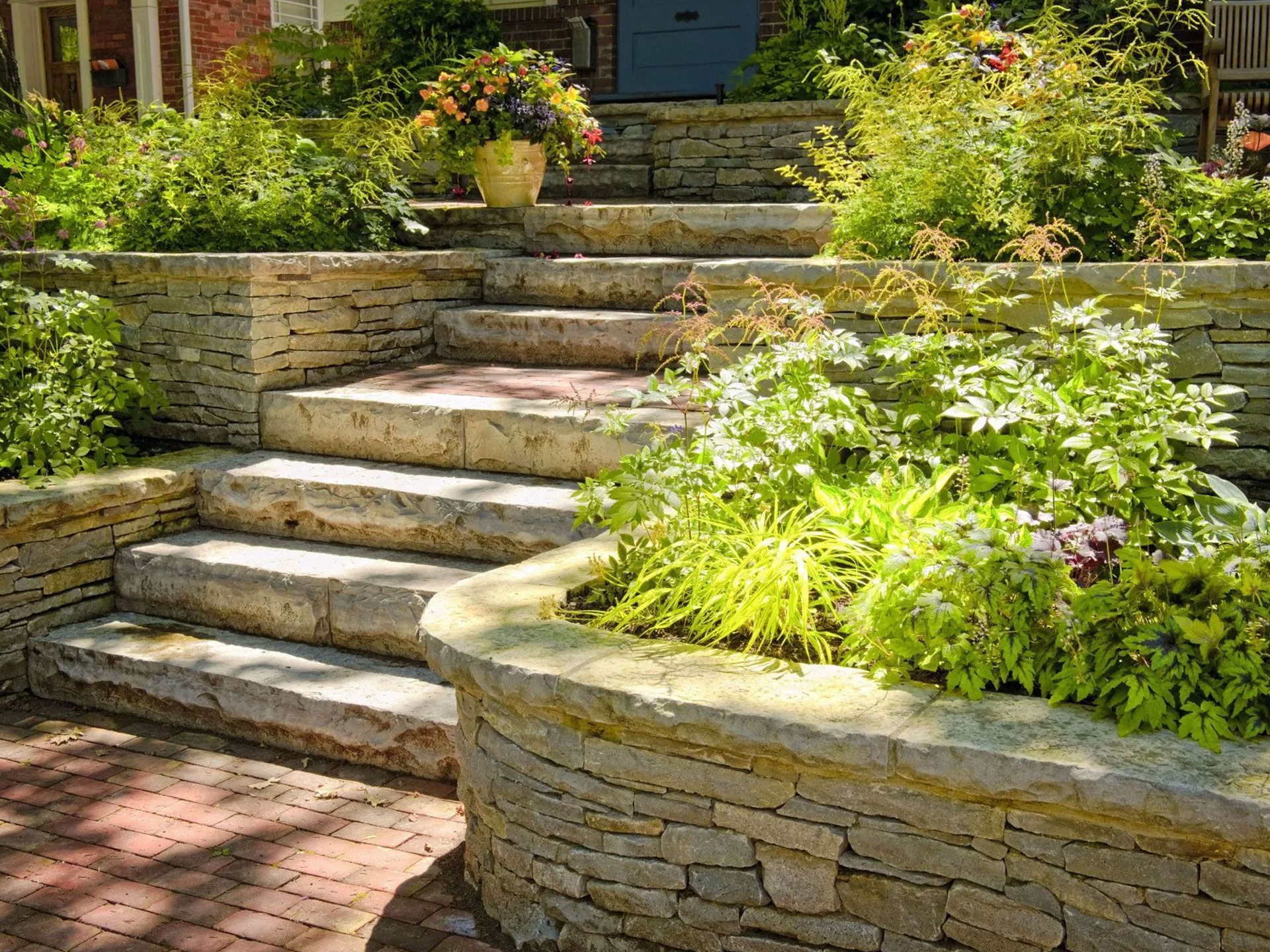 Stone steps leading up to a house, surrounded by plants and a flower pot.
