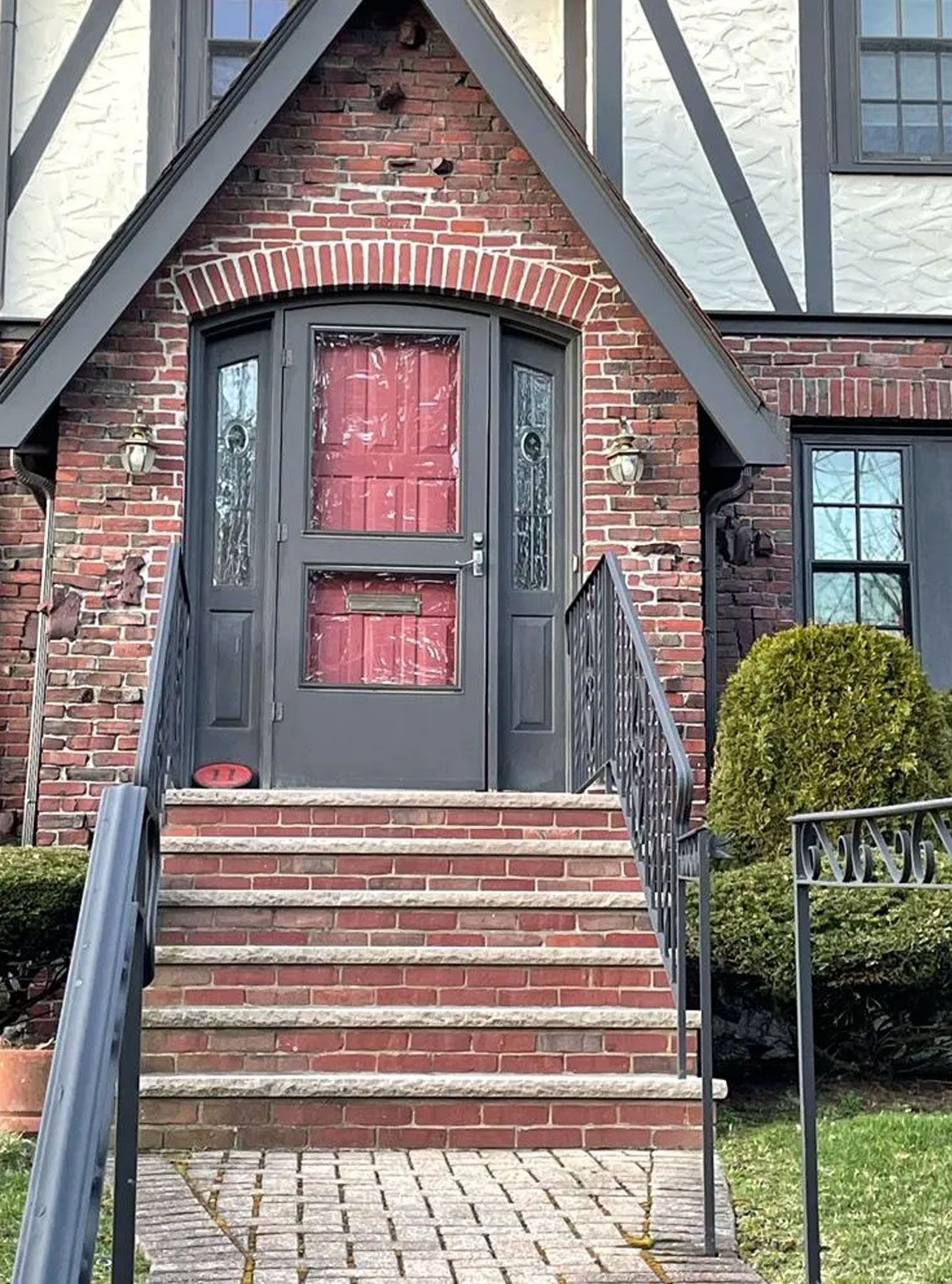 Red brick house entrance with steps, door with screen, black railing, and trim.