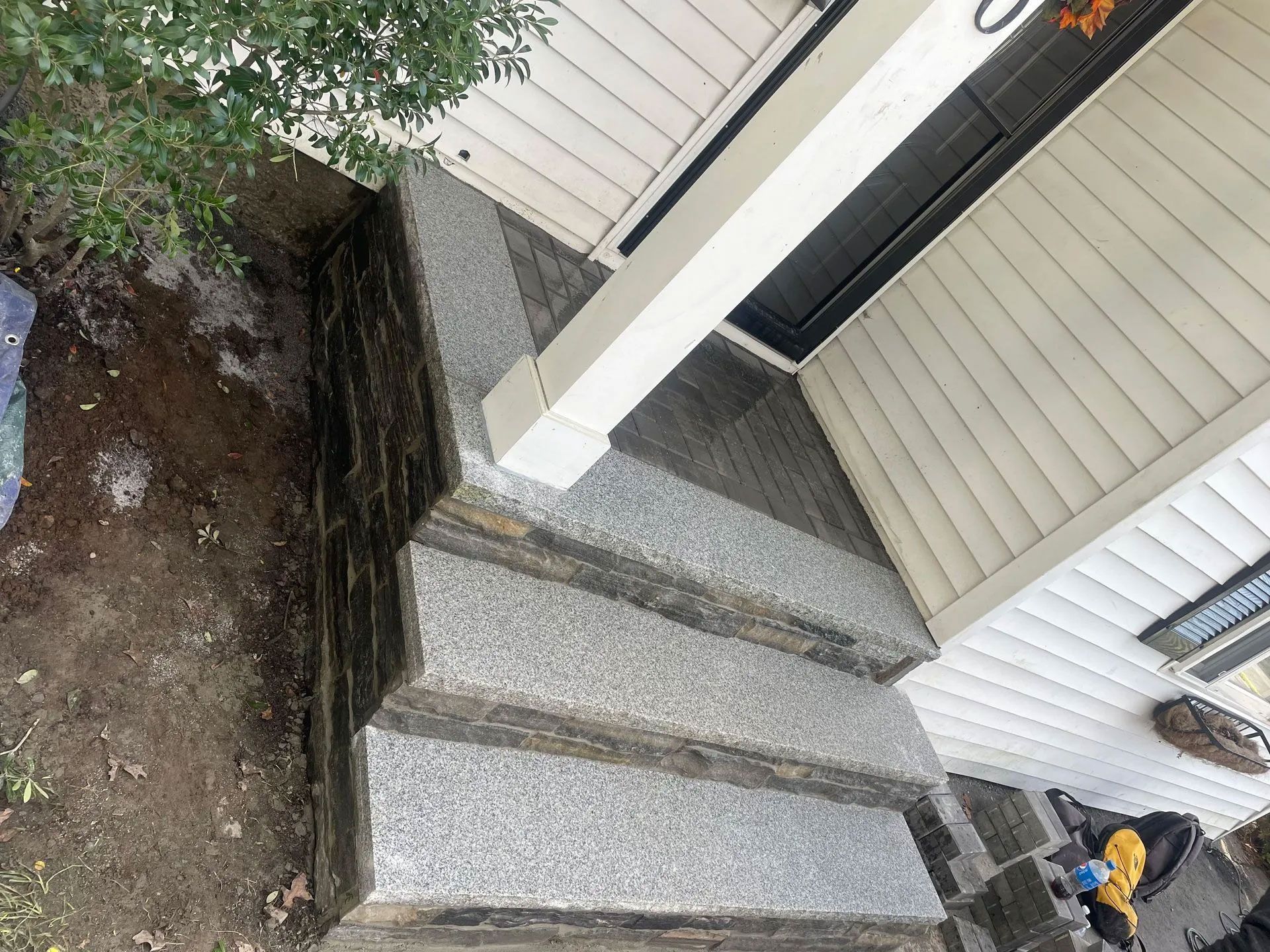 Gray speckled stone steps leading to a house entrance with white siding and a porch column.