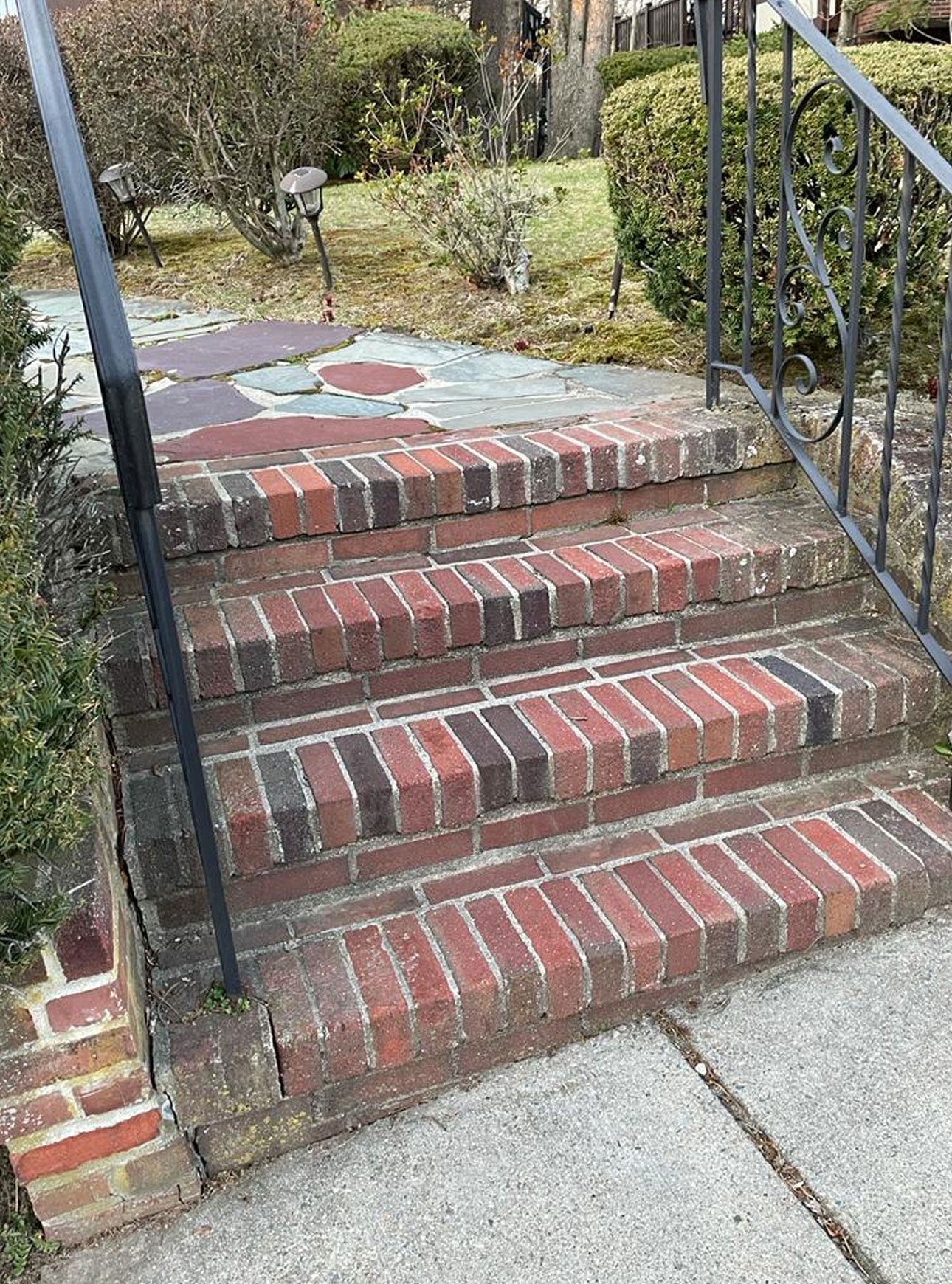 Brick steps leading up to a front yard. Black metal handrail on the right.