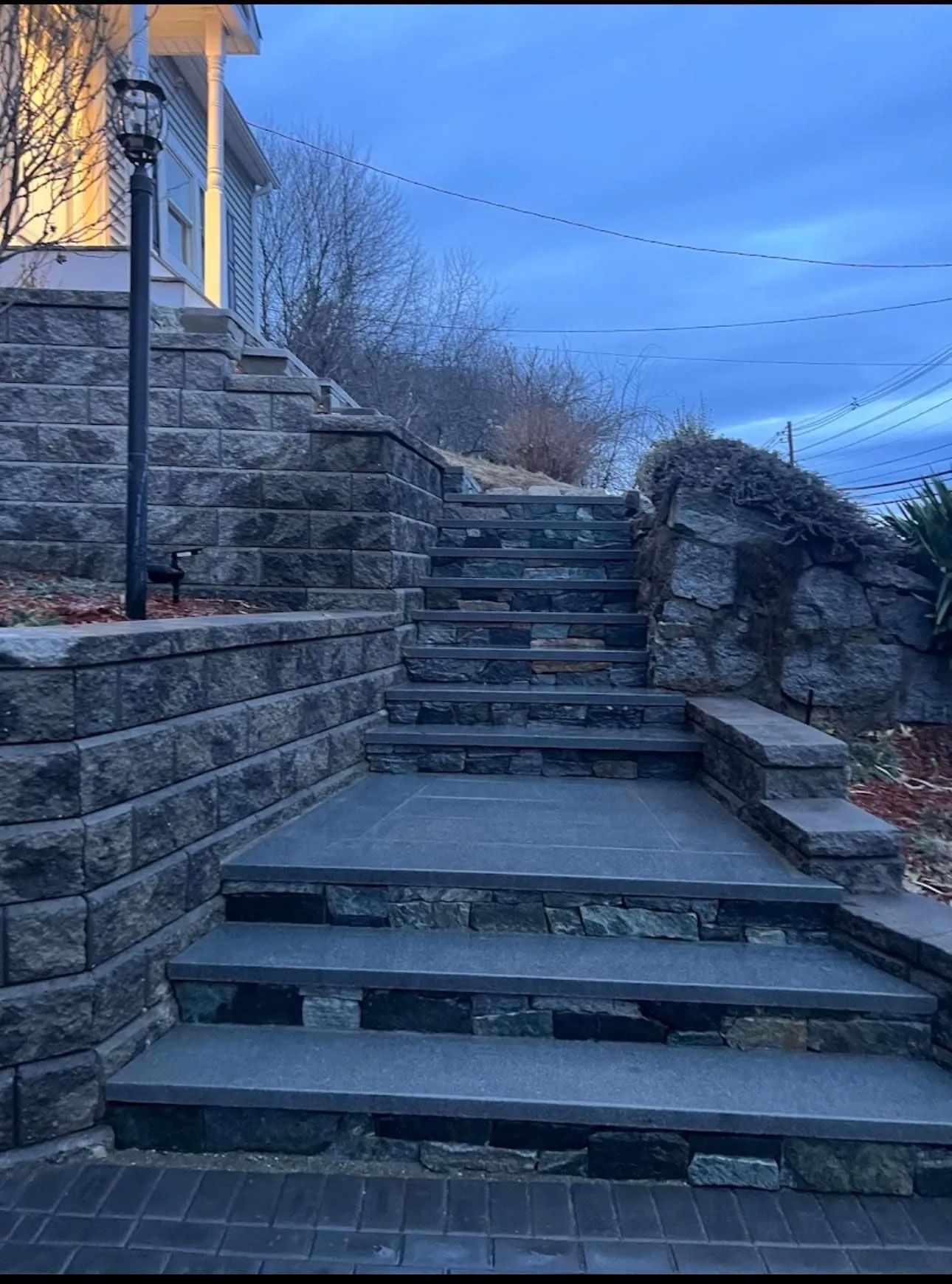 Stone steps and retaining walls leading up to a house, under a dusky sky.