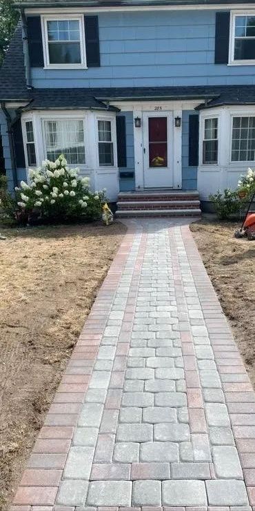 A brick walkway leads to a blue house with white trim and a red door.