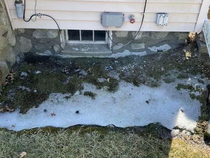 Basement window with stone foundation, grass, and partially melted ice.