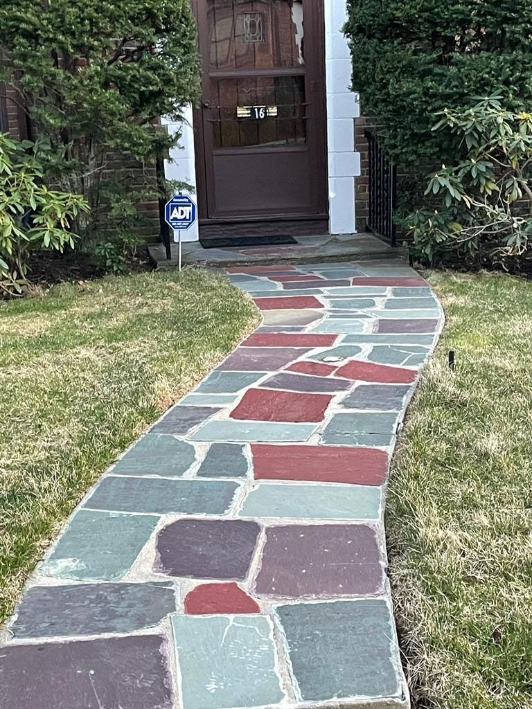 Stone walkway leading to a brown door; green grass and bushes on either side.