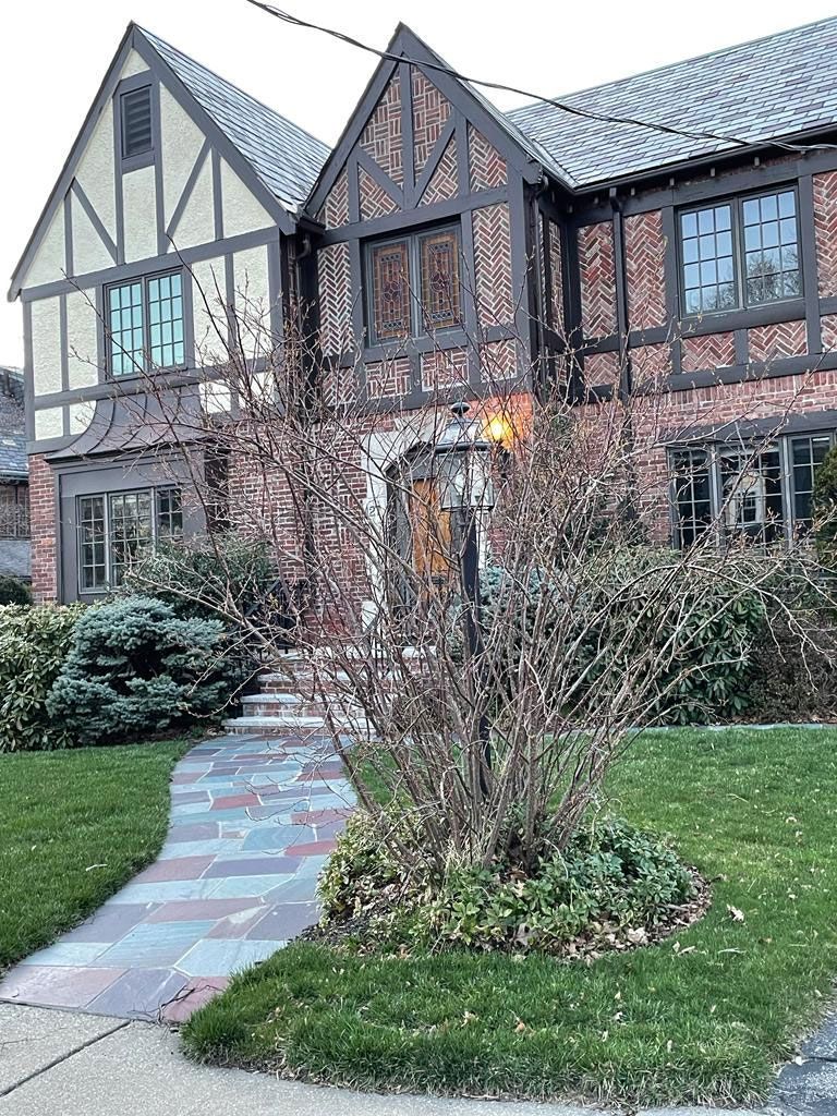 Tudor-style brick and stucco house with a brick path leading to the front door, surrounded by grass and bushes.