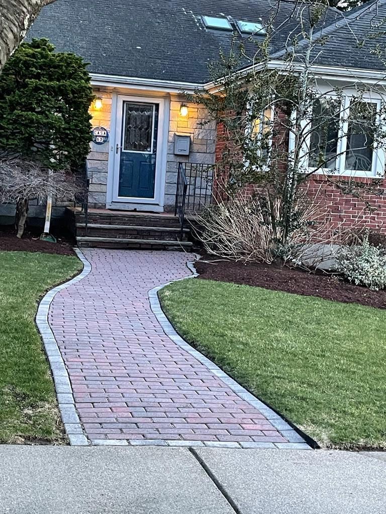 Brick pathway leading to a house with a blue door, surrounded by grass and landscaping.