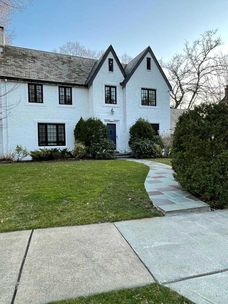 White house with black trim, slate roof, and manicured lawn with a stone path.