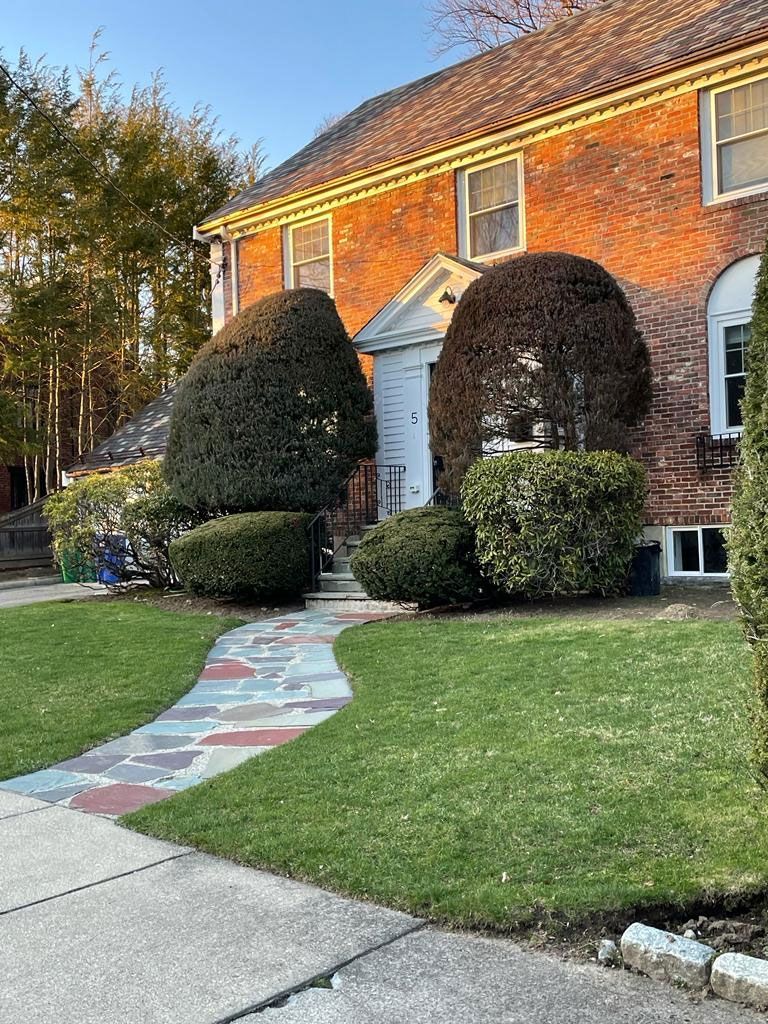 Brick house with a colorful stone walkway leading to the front door, flanked by trimmed bushes and green lawn.