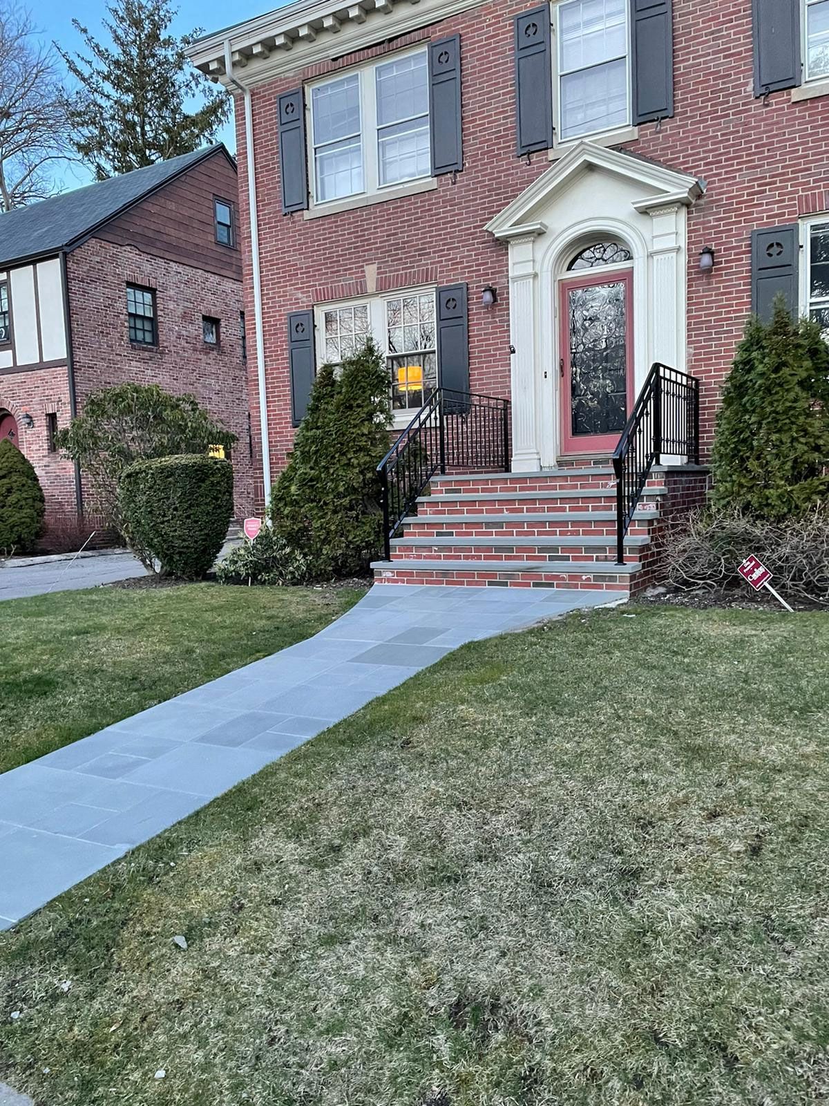 Brick house with a paved walkway, steps, and front door. Green grass surrounds the home.