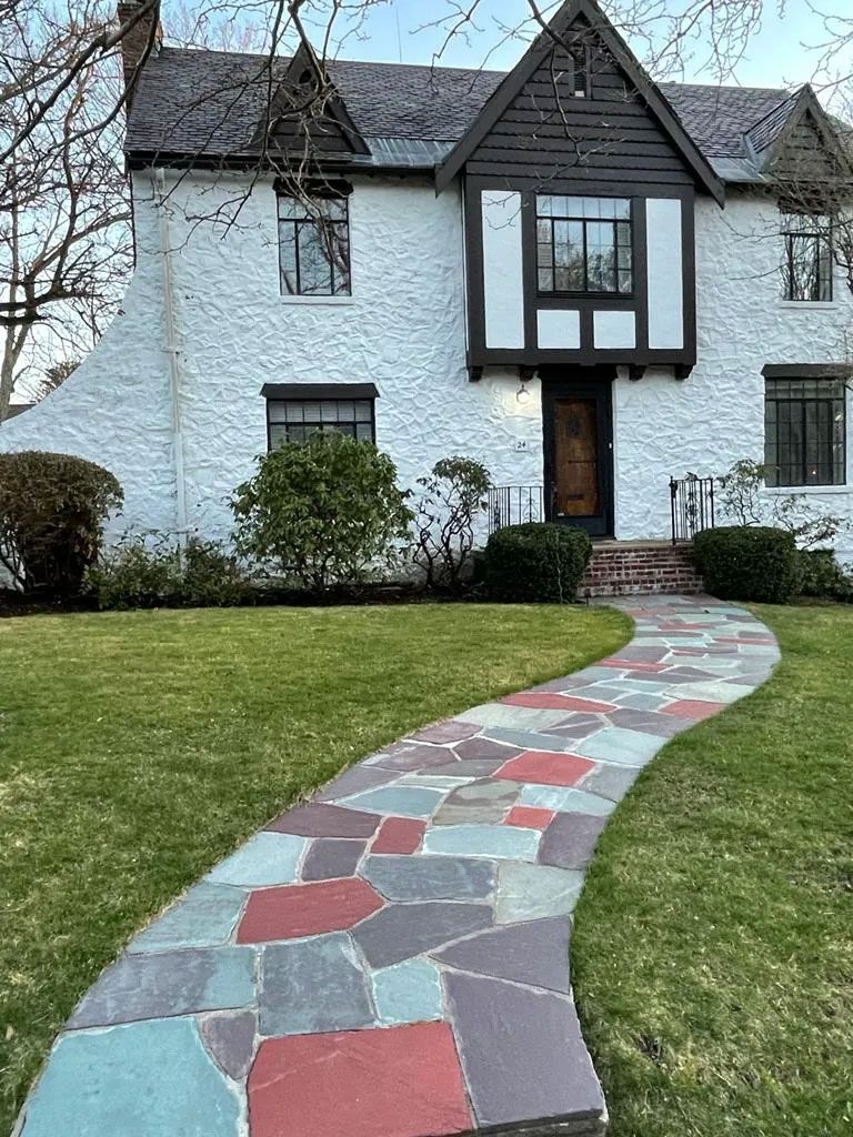 Stone path leads to a white two-story house with dark wood trim, a front lawn, and a blue sky.