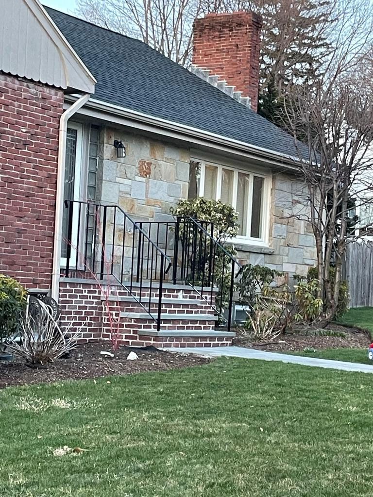 Brick and stone house with steps and black railing leading to a front door.