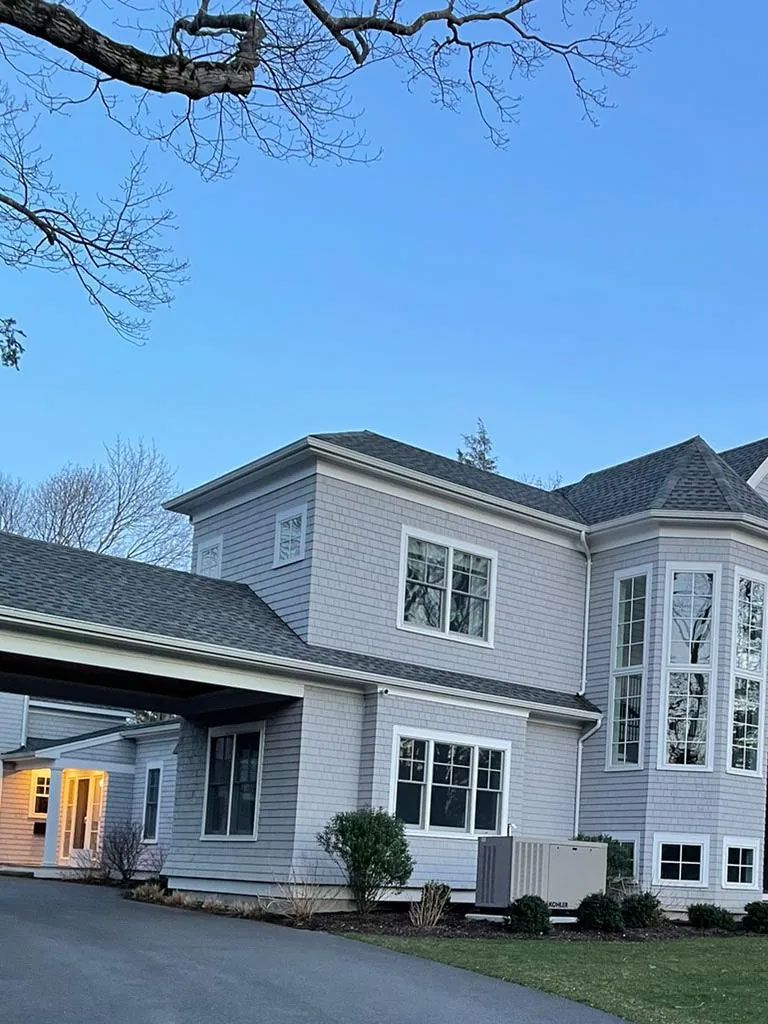 Gray shingled house with a covered walkway and multiple windows against a blue sky.