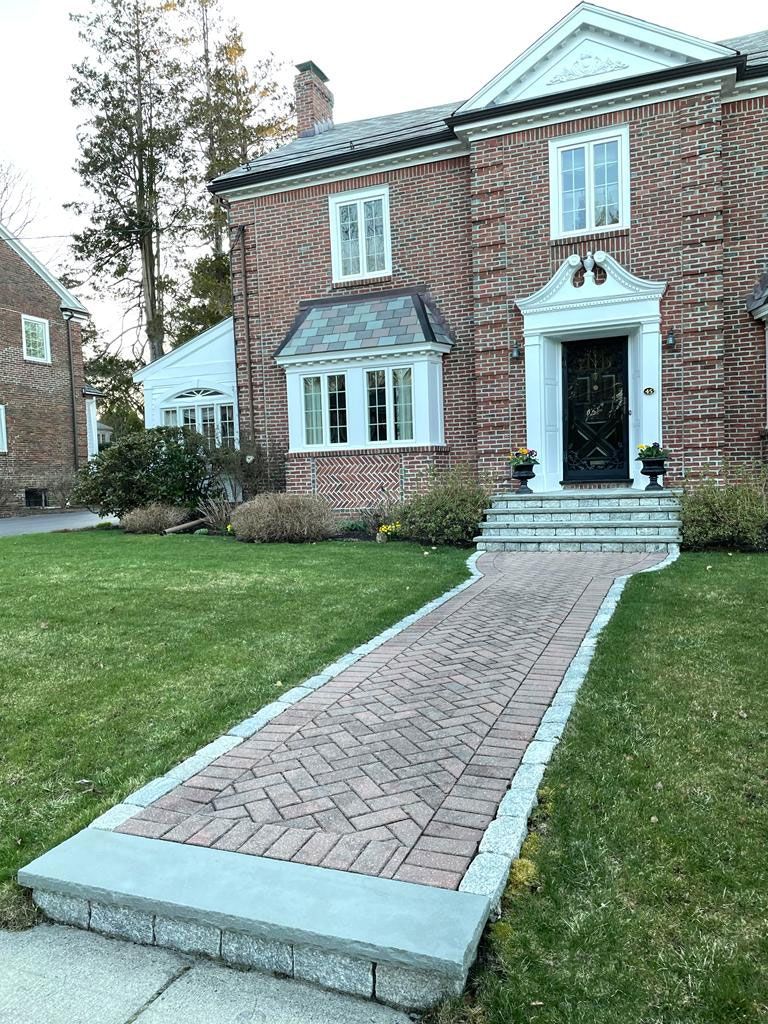 Brick house with brick pathway leading to the front door. Green lawn, trees, and overcast sky.