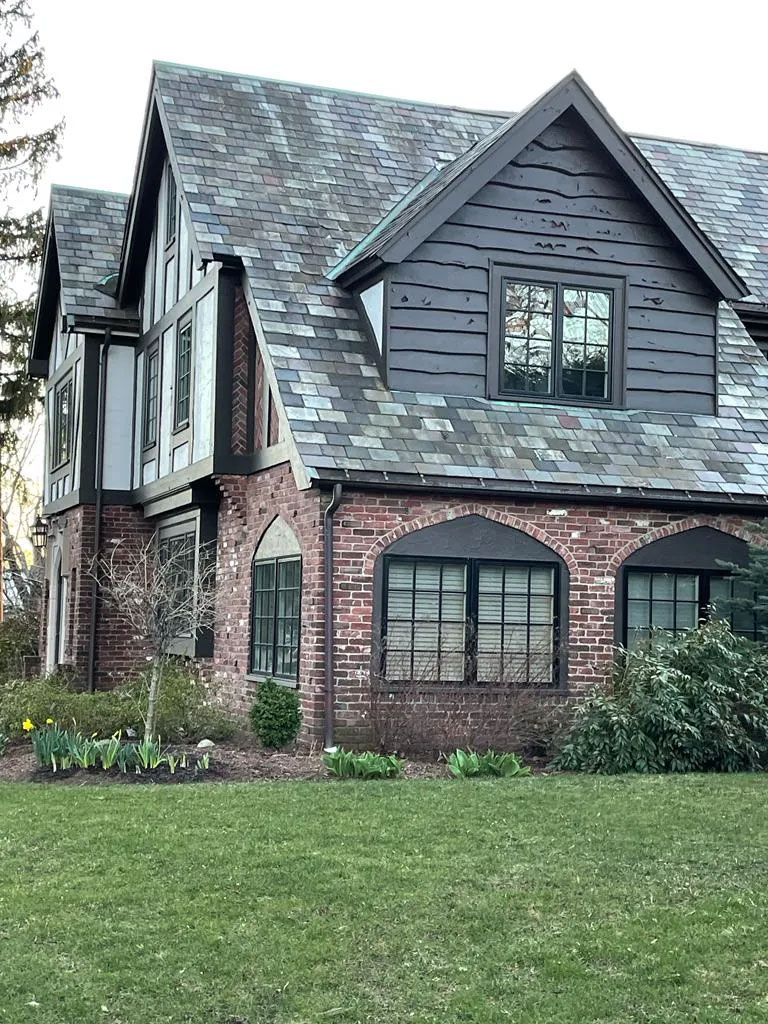 Tudor-style brick house with dark roof and trim, arched windows, and a green lawn.
