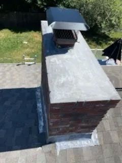 Brick chimney with a metal cap on a shingled roof.
