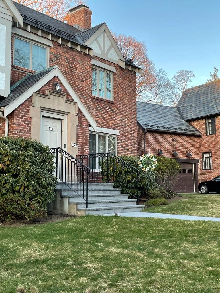Brick house with steps, black railing, and green lawn.