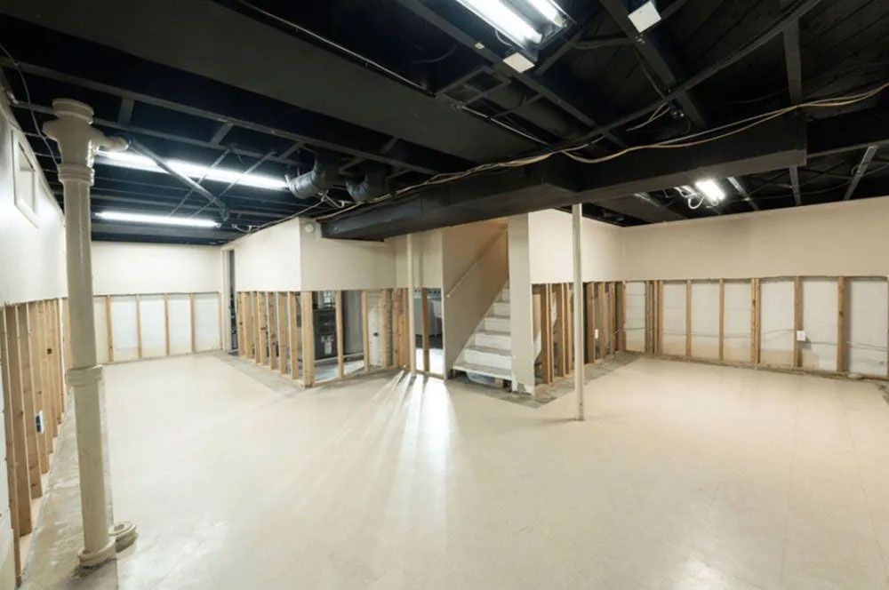 Unfinished basement with exposed wall studs, white walls, black ceiling, and stairs.