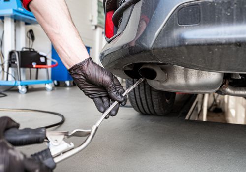 A person is working on the exhaust pipe of a car in a garage.