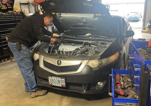 A black car is parked in a garage with its hood open.