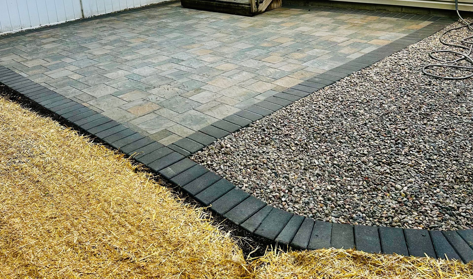 Gravel and tan paver walkway bordering a white fence and house wall