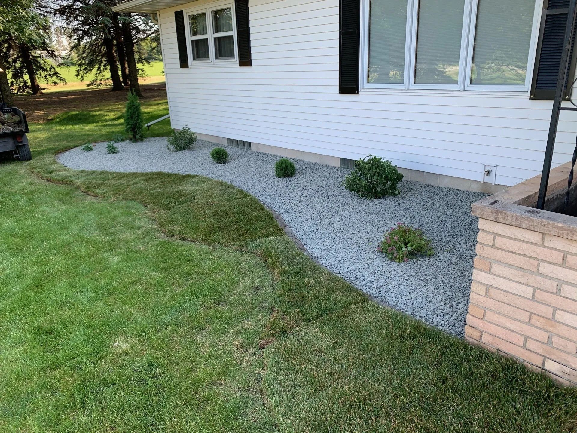 A white house exterior with a curved landscaping bed filled with grey gravel and small green shrubs.