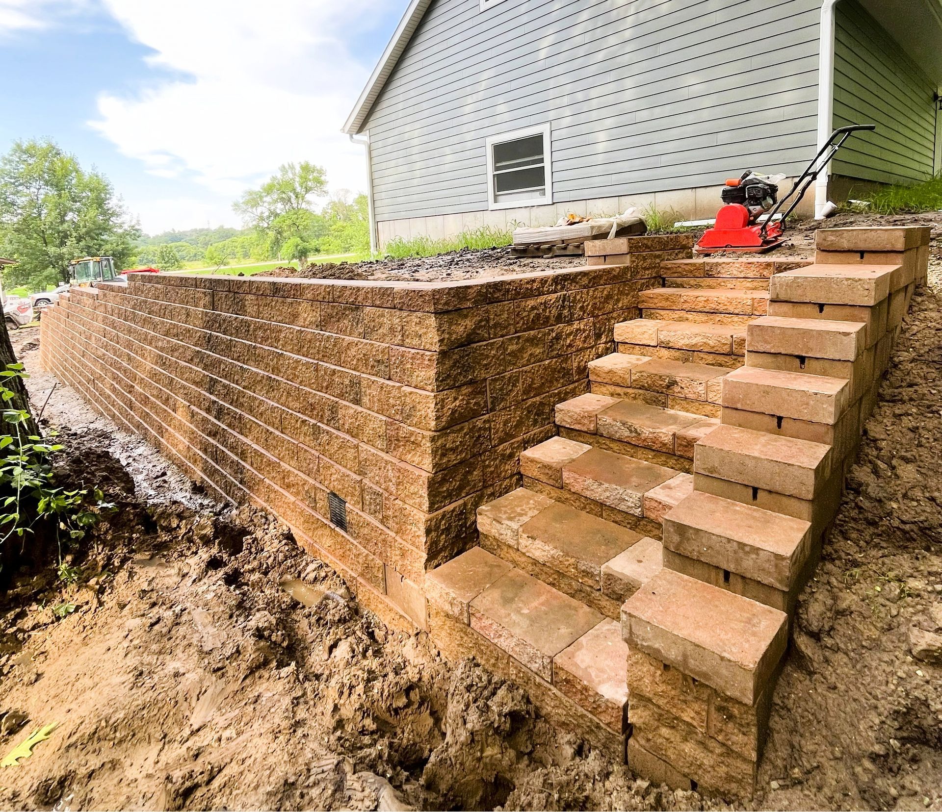 Brick retaining wall and steps beside a house, with a red wheelbarrow on the landing.