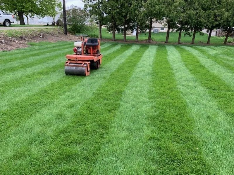 An orange lawn striping mower on a freshly striped green lawn with trees in the background.