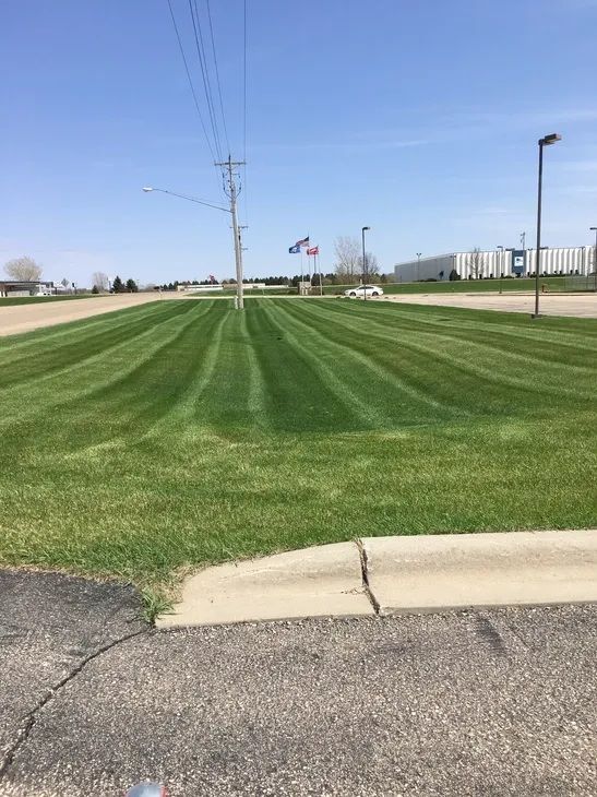 A manicured, striped green lawn stretches toward a utility pole and flags under a bright blue sky.