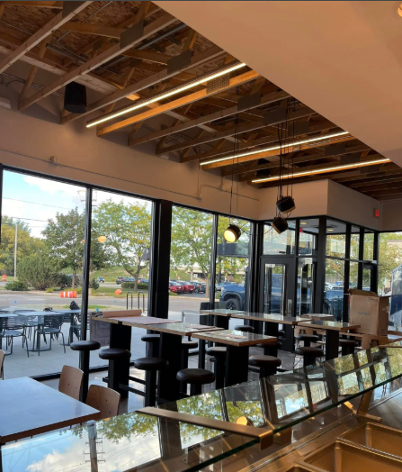Interior of a modern restaurant with large windows, wood ceiling, tables, and stools.