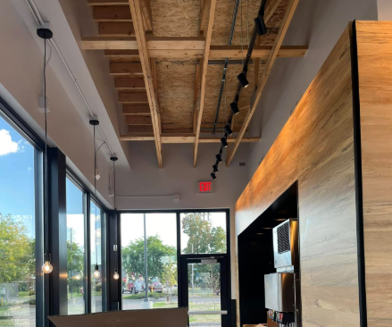 Interior view of a commercial space with open ceiling, large windows, and track lighting.