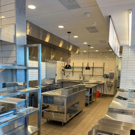 Stainless steel kitchen with cooking equipment, tiled walls, and hanging lights.