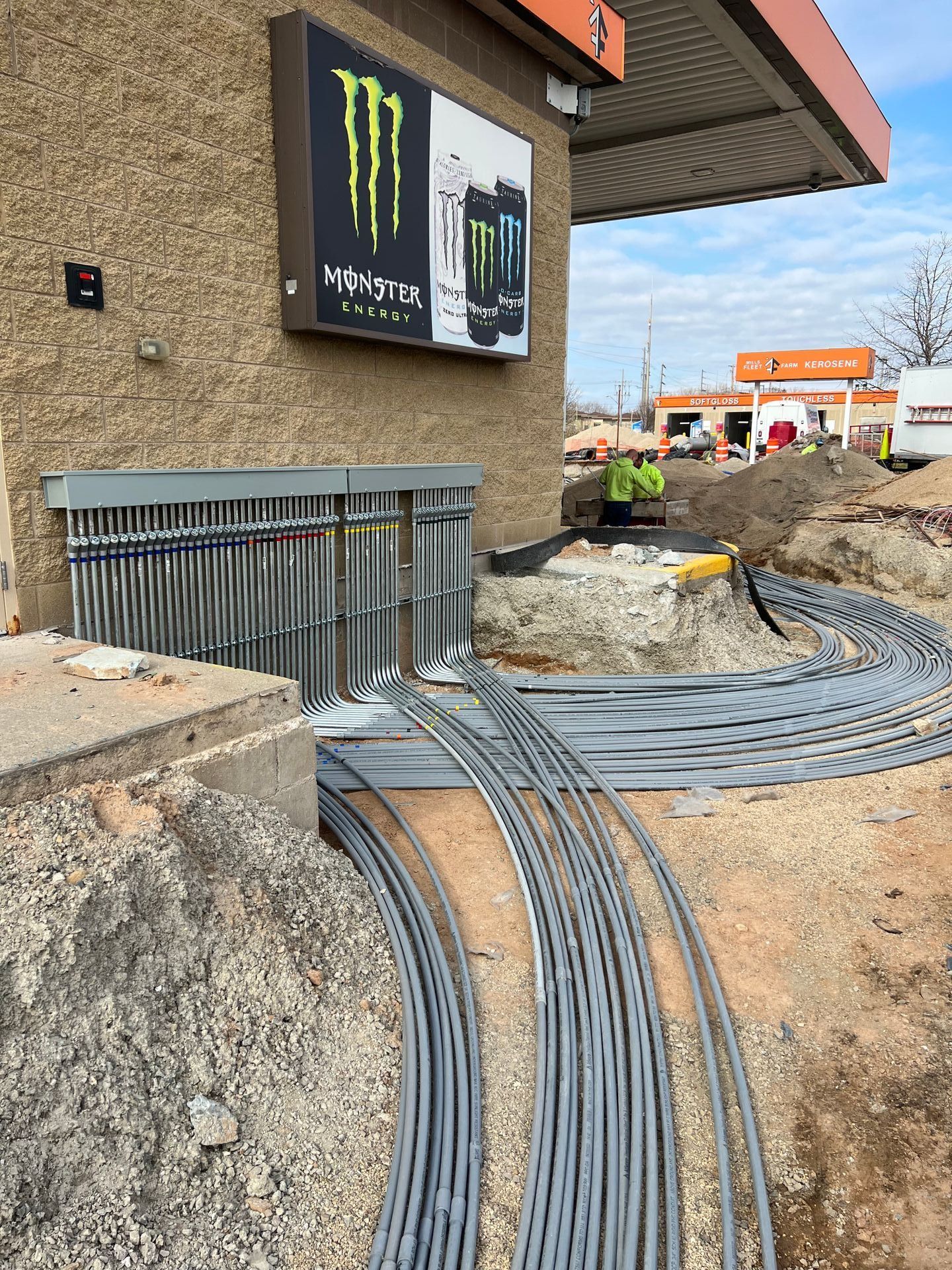 Construction site with wiring, a Monster Energy drink sign, and workers.