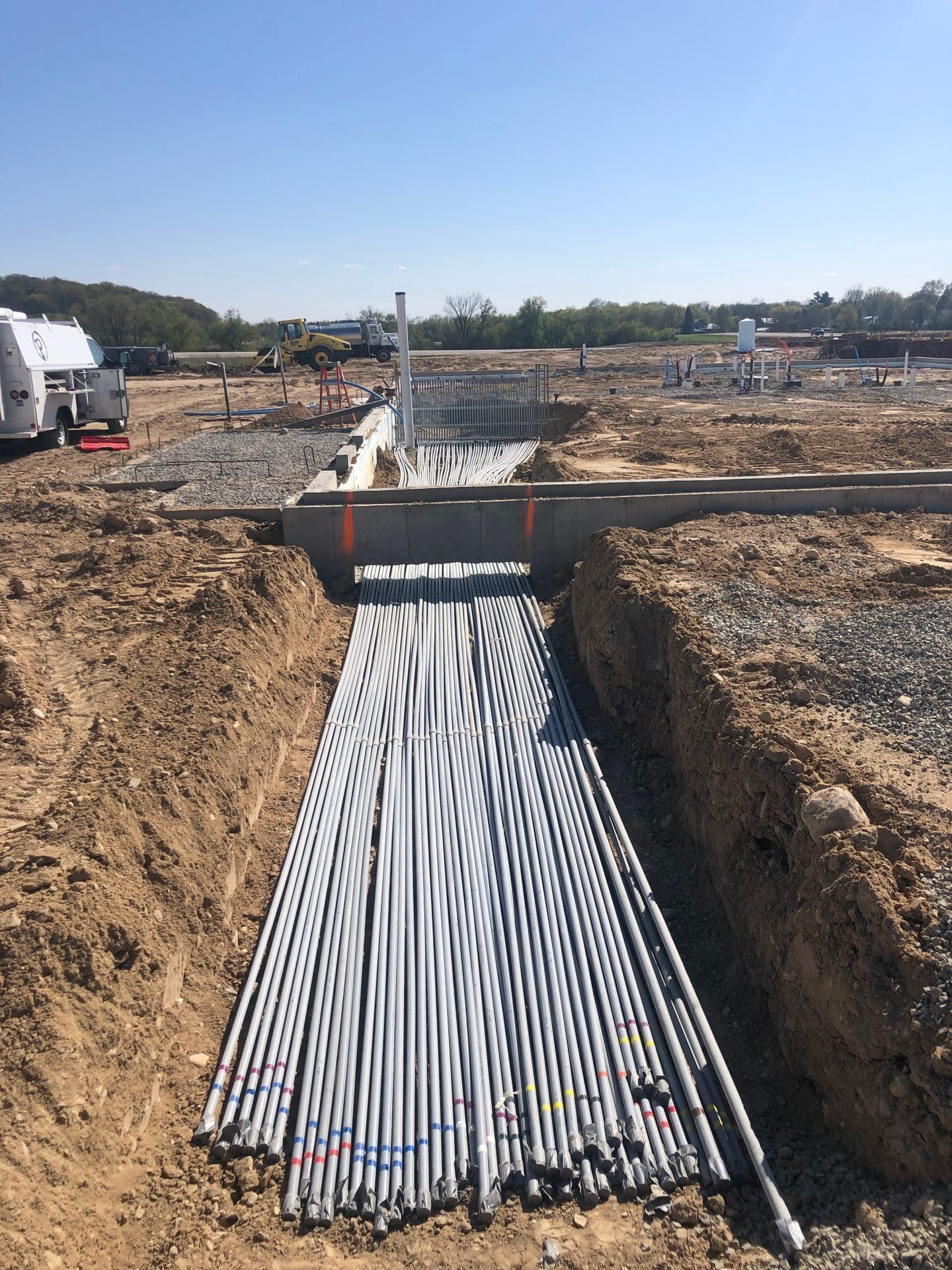 Electrical conduit pipes laid in a construction trench, next to concrete structure on a sunny day.