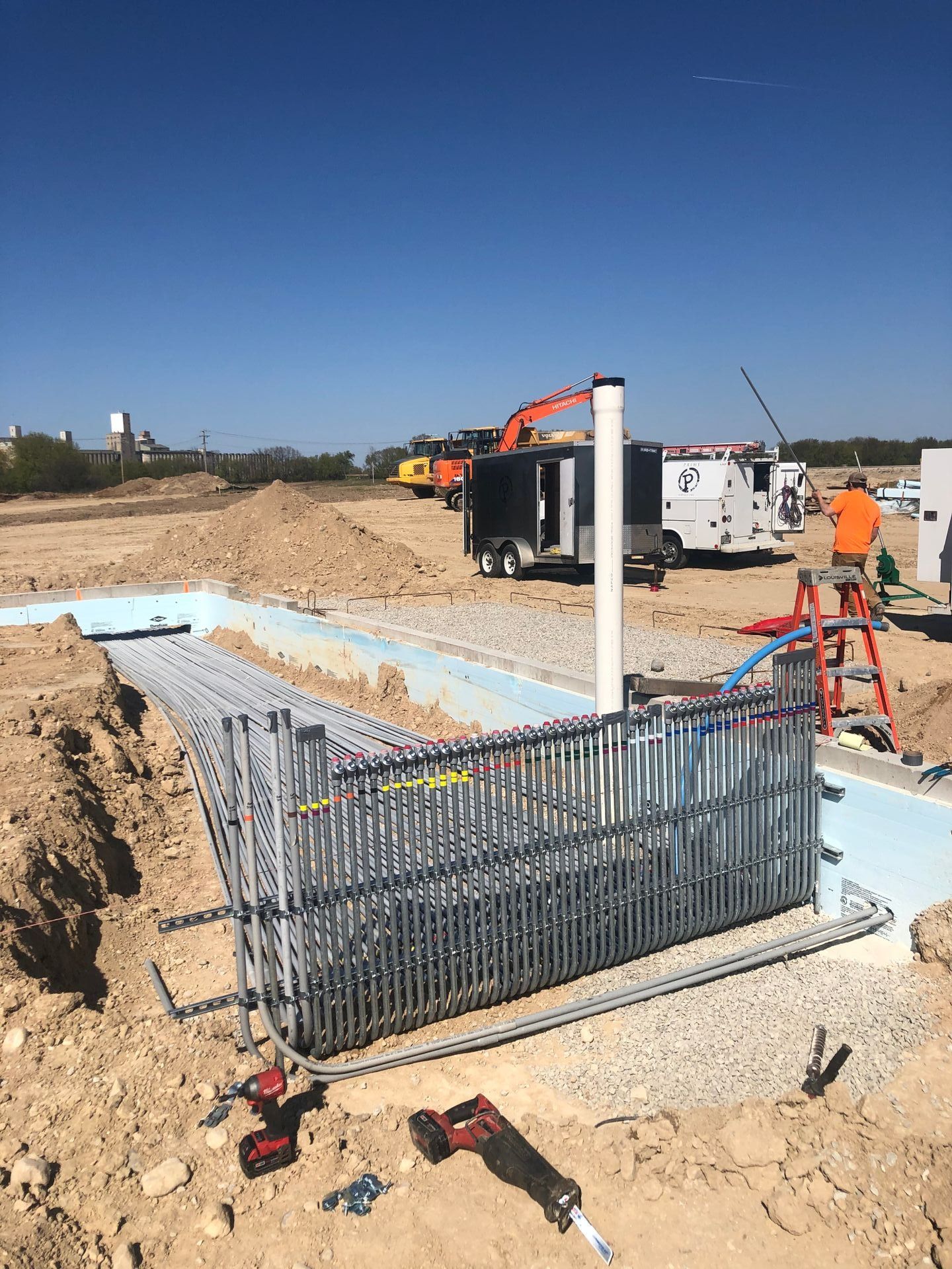 Construction site with metal framework, pipes, and a worker on a ladder.