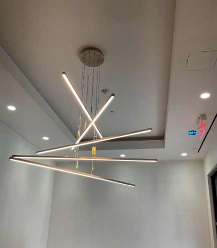 Modern chandelier with horizontal and angled light bars hangs from a white ceiling in a room.