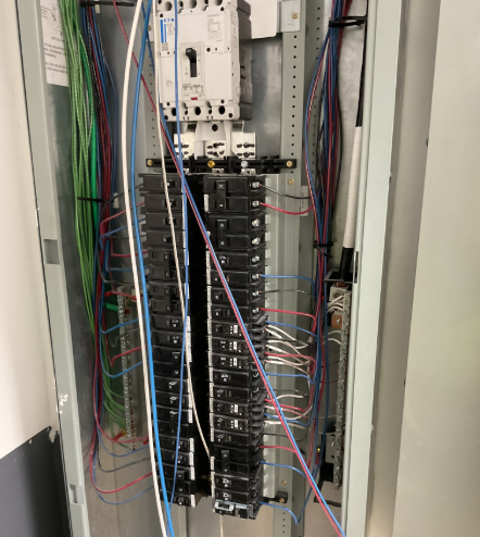 Electrical panel with circuit breakers and wires of various colors.
