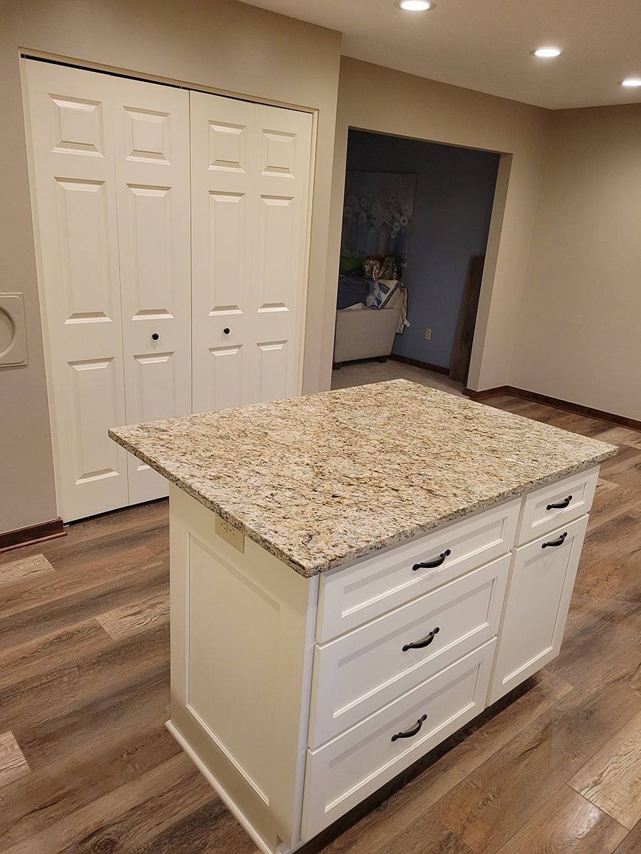Kitchen island with granite countertop and white cabinets, hardwood floors, and a pantry.