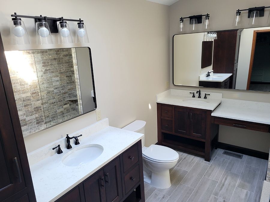 Bathroom with dark wood vanities, white countertops, black fixtures, mirrors, and light fixtures.