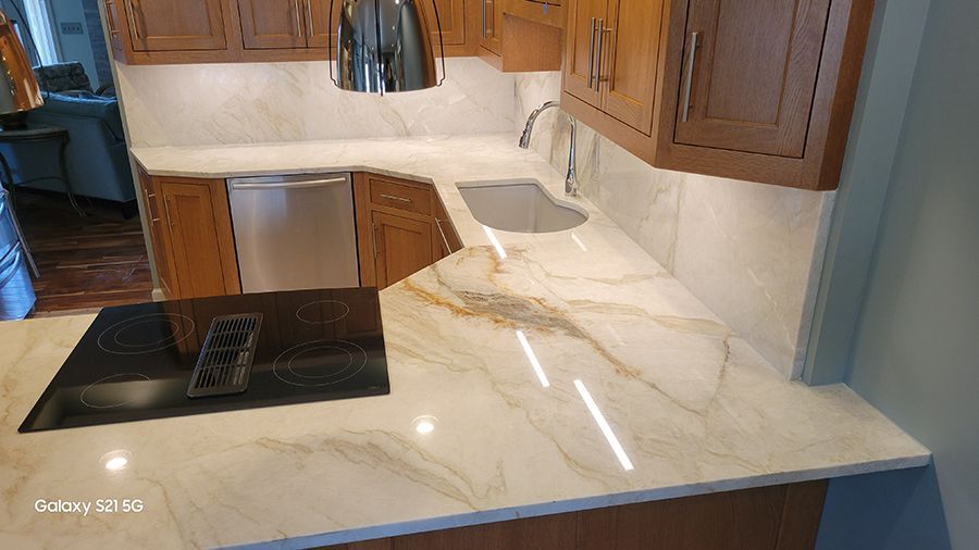Kitchen countertop with cooktop, sink, cabinets, and backsplash with marble-like pattern.