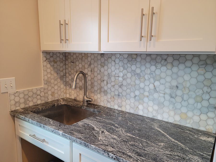 White cabinets and sink with granite countertop and hexagon tile backsplash.