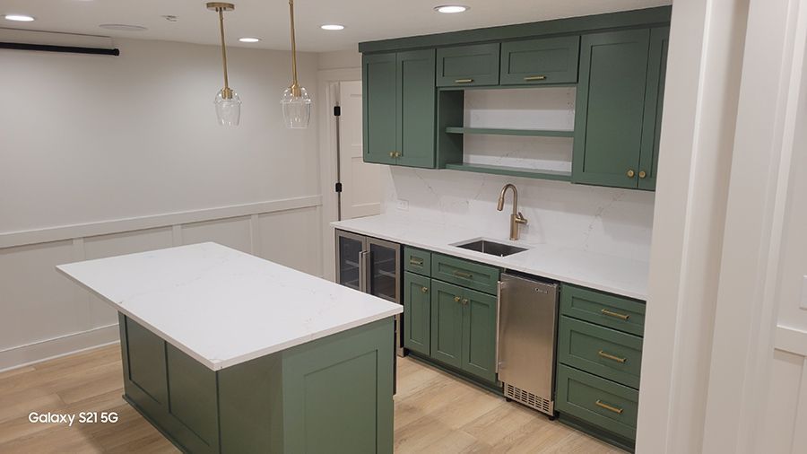 Green cabinets and island in a kitchen, with white countertops, and gold fixtures.